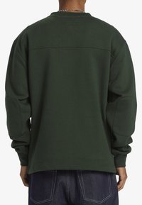 Mörkgrön sweatshirt med rundad halsringning, oversized passform och armbågsfälgar. Tillverkad av mjukt tyg med en slät textur.