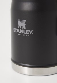 Musta eristetty juomapurkki, jossa on ruostumattomasta teräksestä valmistettu pohja. Kannen päällä on hopeinen logo "STANLEY" ja "SINCE 1913". Mattapintainen pinta.