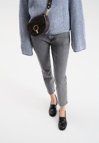 Szare dżinsy, jasnoniebieski sweter z dzianiny, czarna torba na ramię z złotym wykończeniem i czarne buty bez zapięcia dopełniają całość.