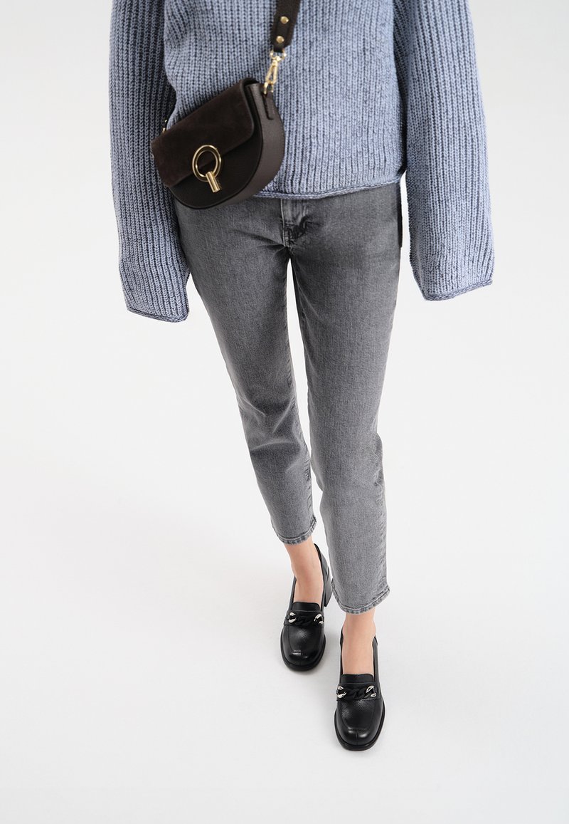 Szare dżinsy, jasnoniebieski sweter z dzianiny, czarna torba na ramię z złotym wykończeniem i czarne buty bez zapięcia dopełniają całość.