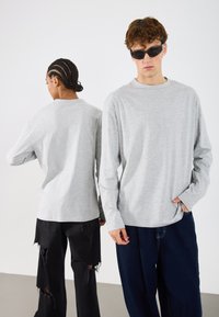 Lys grå langermet skjorte med rund hals, vist fra front og bak, sammen med slitte svarte og mørke denimbukser.