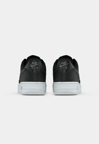 Crne Nike Air tenisice s teksturiranom tkaninom, bijelim srednjim potplatima i utisnutim brendingom na peti i jeziku. Klasična niska silueta.