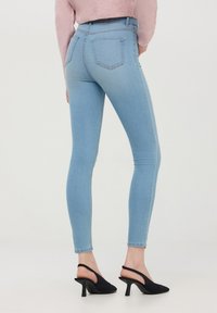 Dżinsy typu skinny w jasnoniebieskim deni, z wysokim stanem, pięcioma kieszeniami i delikatnym blaknięciem na udach. W zestawie z czarnymi butami na obcasie.