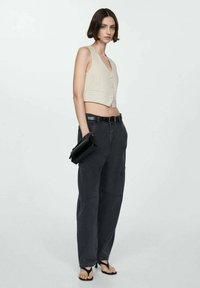 Beige ribbed cropped vest with buttons, paired with loose-fit dark gray cargo pants and black heeled sandals, holding a small black bag.