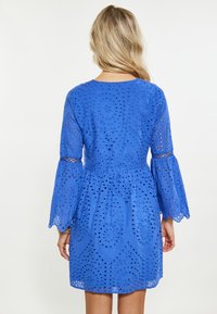 Rochie albastră din dantelă cu mâneci lungi și evazate, având un model tăiat circular și floral, și o talie ajustată care se transformă într-o fustă evazată.