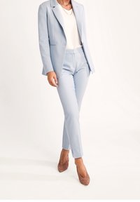 Jasnoniebieska żakietowa marynarka i pasujące dopasowane spodnie z gładkiego materiału, zestawione z białą bluzką i beżowymi szpilkami.