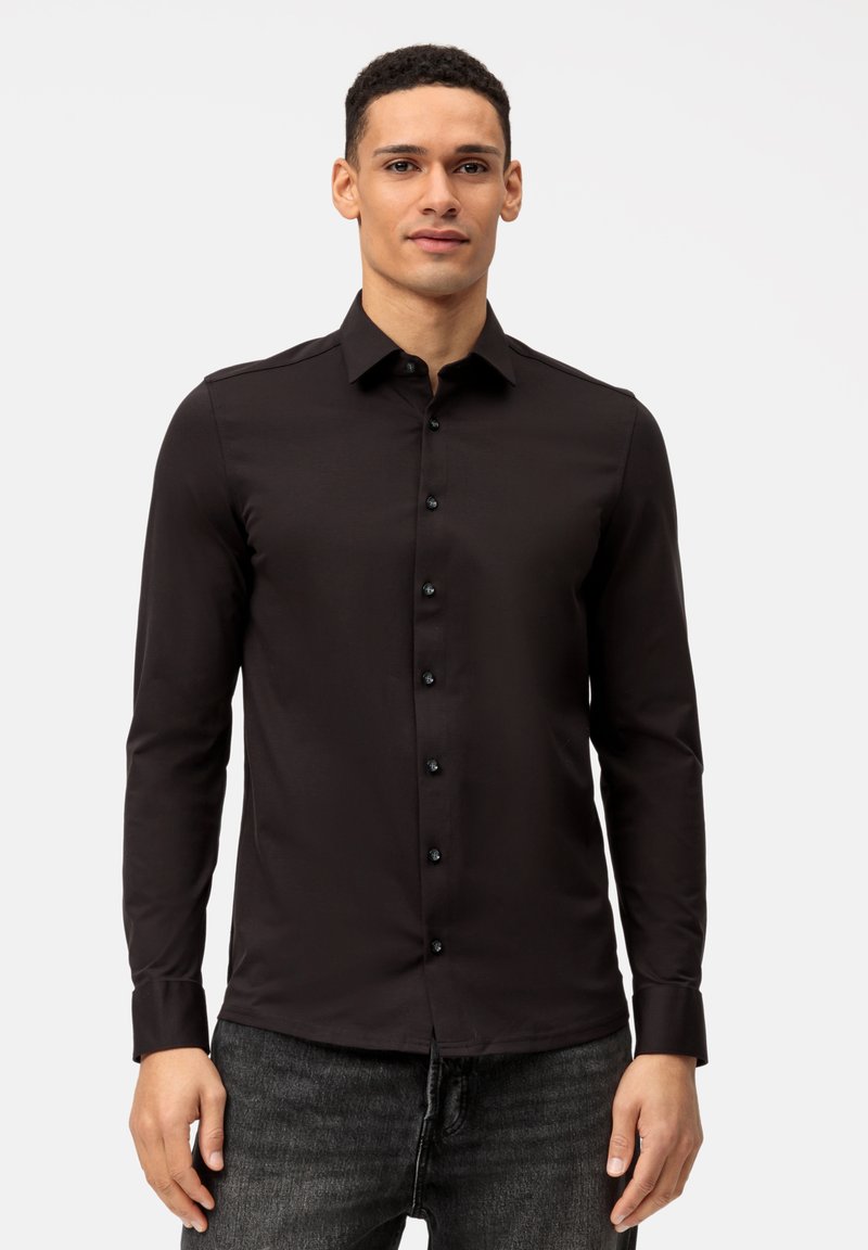 Camicia nera a maniche lunghe con colletto, dotata di bottoni neri e design aderente, indossata con jeans scuri. Tessuto liscio.