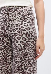 Παντελόνι σε φαρδιά γραμμή με λεοπάρ σχέδιο σε μπεζ χρώμα με μαύρες και ροζ κηλίδες. Δ ιαθέτει μπροστινές τσέπες και κλείσιμο με κουμπί. Ορατό υφή υφάσματος.