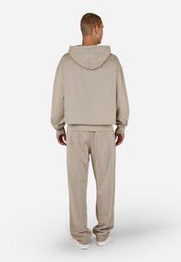 Bežová mikina s kapucňou a voľným strihom, so zúženými manžetami a zodpovedajúcimi zúženými nohavicami. Vyrobená z mäkkej tkaniny, s minimálnymi švami a detailmi.