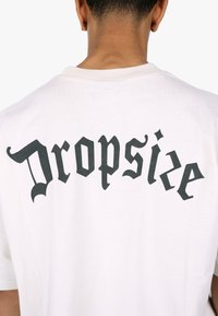 Hvit bomulls T-skjorte med dristig svart gotisk stiltekst som står "Dropsize" på baksiden. Korte ermer og klassisk rund halsdesign.