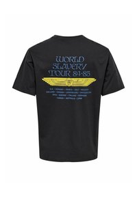 Sort bomulds T-shirt med blå og gul tekst på bagsiden: "WORLD SLAVERY TOUR 84-85" med et vinge grafik og navne på byer opført.