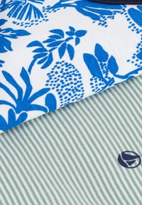 Twee stofstalen: de ene met een blauw bloemenpatroon op een witte achtergrond, de andere groen met subtiele strepen en een logo.