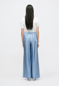 Pantalones anchos de satén azul claro con cinturilla elástica, combinados con una camiseta blanca de manga corta, vistos desde atrás.