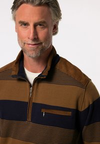 Braun und marineblau gestreifter Pullover mit einem Reißverschluss-Kragen, ausgestattet mit einer Brusttasche und texturiertem Stoff. Geripptes Material mit Kontrastdetails.