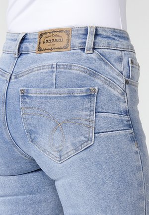 Jeans de mezclilla azul claro con cintura baja, que presentan una etiqueta de cuero, costuras decorativas en los bolsillos y un diseño ajustado.