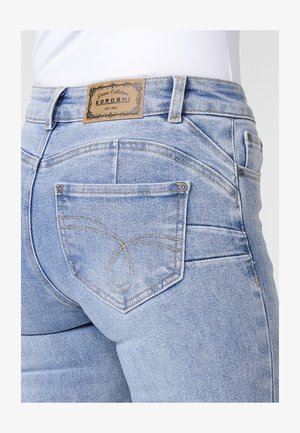 Gai zils denim stils ar zemu vidukli, ar ādas birku, dekoratīvo izšuvumu uz kabatām un piegulošu dizainu.