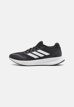 Shoe desportivo preto com parte superior em malha, bico redondo e três riscas brancas de lado. Sola leve com sola de borracha texturizada para aderência.