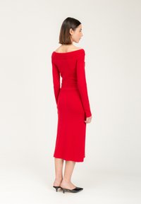 Rotes Off-Shoulder-Kleid mit eng anliegendem Oberteil und Rippendetails. Mittellanges Design, weicher Stoff, kombiniert mit schwarzen spitzen Ballerinas.
