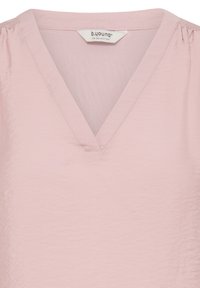 Světlounce růžová halenka s výstřihem do V, měkkou texturou a nařasením na ramenou. Vyrobena z lehké látky, s minimálním množstvím švů.