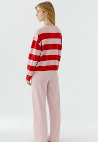 Gestrickter rot-rosa gestreifter Pullover mit lockerem Schnitt, kombiniert mit hellrosa gerippten weiten Hosen. Weiche Textur und lässiges Design.