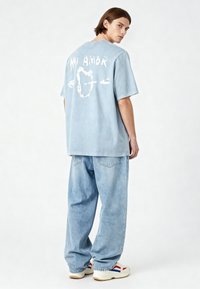 T-shirt oversize blu chiaro con testo grafico bianco "MI AMOR" e un cuore, abbinato a jeans larghi blu chiaro e sneakers bianche.