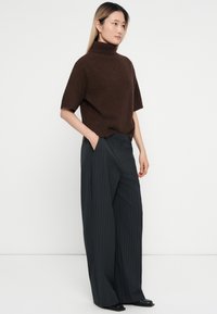 Rudas trumpas rankovės golfo megztinis derinamas su juodais dryžuotais plačiais kelnais ir juoda avalyne, pasižymintis laisvu siluetu ir minkšta tekstūra.