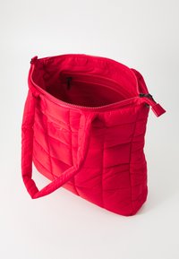 Sac cabas matelassé rouge avec fermeture zippée en haut, deux poignées et une poche zippée intérieure. Fabriqué en matériau lisse et rembourré.
