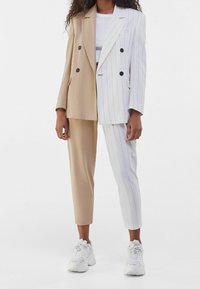 Beige och vit randig oversized blazer med matchande skräddarsydda byxor, med dubbelknäppt design och rund svarta knappar. Vita sneakers.