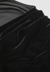 Czarna aksamitna tkanina o miękkiej, teksturowanej powierzchni, z naturalnymi fałdami i drapowaniami. Gładkie tło z minimalnym połyskiem.