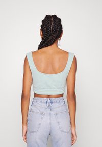 Jasnoniebieski krótki top na szerokich ramiączkach, z prążkowanym wykończeniem i gładką teksturą, noszony z wysokim stanem, z przetartymi dżinsami.