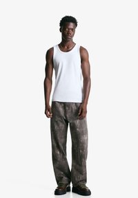 Hvid bomulds tanktop parret med løse, grå strukturerede bukser. Modellen har mørke chunky sko på med grønne snørebånd. Enkel design, neutrale farver.