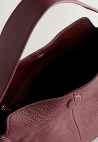 Sac à main en cuir mauve foncé ouvert, montrant un extérieur texturé, une anse large et une poche intérieure zippée.
