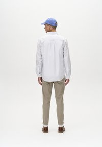 Camisa de rayas blanca y azul de manga larga, pantalones caqui y una gorra azul claro. La camisa tiene puños ajustados y un dobladillo curvado. Zapatos marrones en exhibición.