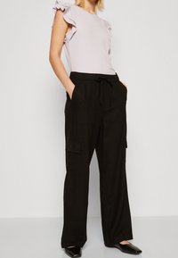 Černé cargo kalhoty s bočními kapsami, pohodlný střih a nastavovací stahovací pas v kombinaci se světle fialovým topem s krátkým rukávem a volánovými detaily.