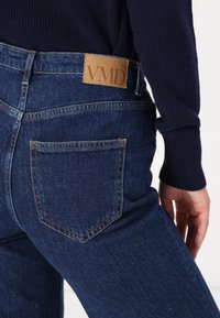 Blauwe spijkerbroek met een hoge taille, voorzien van een tan leren merklabel en klassieke achterzakken gestikt met contrasterend garen.