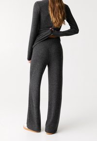 Pull en maille gris foncé et pantalon large en tissu doux. Le haut présente une coupe ajustée, tandis que le pantalon a une silhouette décontractée.