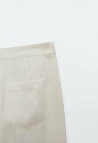 Achteraanzicht van beige broek met een enkele achterzak en riemlussen tegen een effen witte achtergrond.