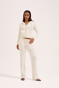 Felpa bianca corta con zip frontale e cordini, abbinata a pantaloni a vita alta coordinati, caratterizzati da cuciture laterali e una vestibilità morbida.