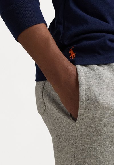 Námornícka bavlnená košeľa s dlhým rukávom a malým oranžovým logom koňa, v kombinácii so šedými bavlnenými teplákmi s vreckami a jemnou textúrou.