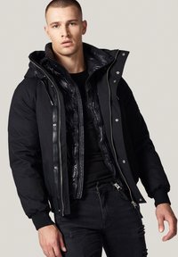 Czarna kurtka puchowa z odpinaną wewnętrzną warstwą, zamek błyskawiczny oraz regulowany kaptur. Posiada ściągacze przy rękawach oraz elegancki, smukły design.