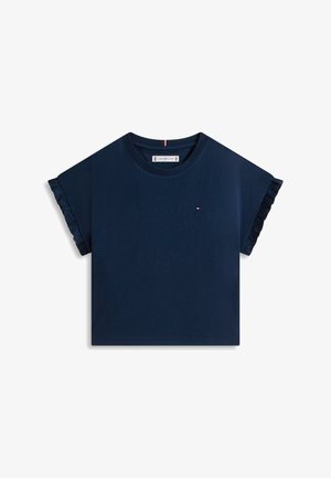 Tumši zils īsroku tops ar volāniem uz piedurknēm, apaļu kaklu un nelielu taisnstūrveida logotipu uz kreisā krūts.