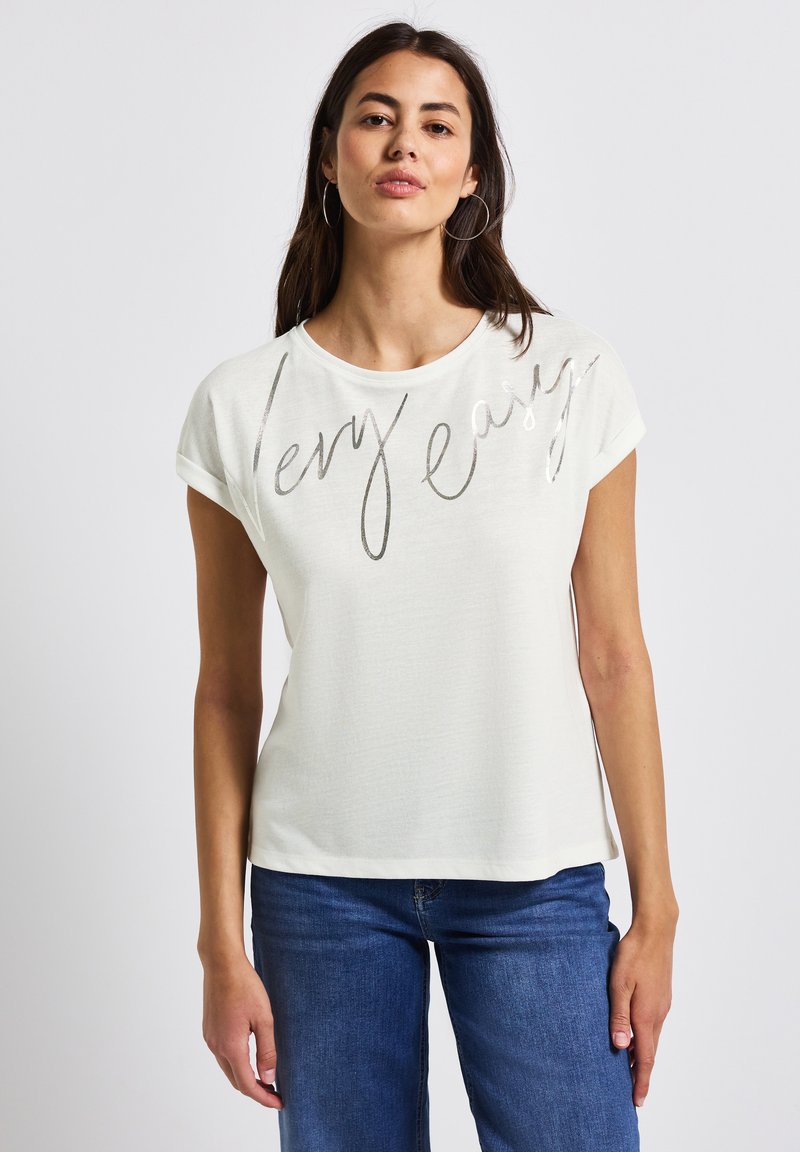 Light beige short-sleeve T-shirt with a round neckline, featuring a metallic silver scripted text "very easy" across the front. Casual fit.