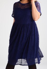 Abito in pizzo blu navy con maniche corte, scollatura ondulata e gonna svasata. Presenta motivi floreali e un corpetto aderente.