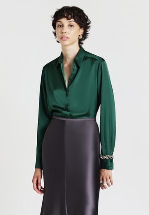 Camicia in seta verde con colletto a punta e maniche lunghe, abbinata a una gonna in satin grigio scuro elegante.