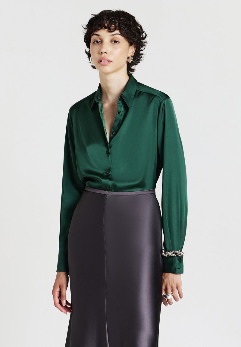Camicia in seta verde con colletto a punta e maniche lunghe, abbinata a una gonna in satin grigio scuro elegante.