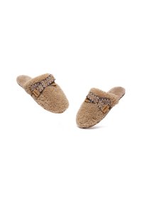 Brown sheepskin slippers with a textured surface, featuring a decorative woven strap and a wooden brand tag. Open back design.