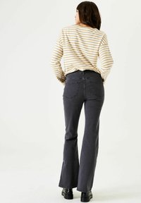 Gestreiftes Langarmshirt mit lockerer Passform, kombiniert mit hochgeschnittenen, dunkelgrauen, ausgestellten Jeans. Das Outfit zeichnet sich durch ein klassisches und lässiges Design aus.