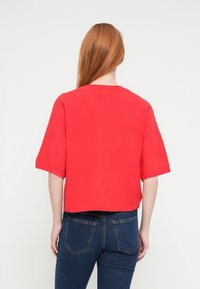 Red short-sleeve top with a round neckline, made of smooth fabric; worn with dark blue denim jeans, showing a casual back view.