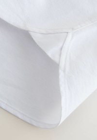 Weiße Baumwollstoff-Ecke mit sichtbarer Naht und Saum, die Textur und gefaltete Kante zeigt.