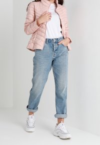 Jasnoróżowa pikowana kurtka z wysokim kołnierzem, biała koszulka i podwinięte jasnoniebieskie jeansy. Dobranie do tego białe trampki z czerwonymi akcentami.